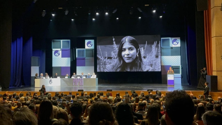 Auditorio con muchas personas en su interior y una foto de una chica en la pantalla grande