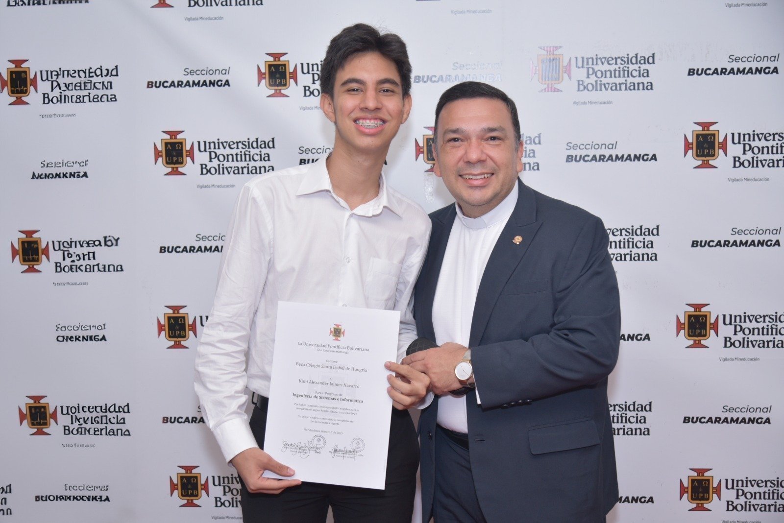 Estudiante beneficiado con la Beca de Honor de la Universidad Pontificia Bolivariana Seccional Bucaramanga recibe su reconocimiento de manos del rector, el Presbítero Gustavo Méndez Paredes, durante la Ceremonia de Becas de Honor, un evento que destaca la