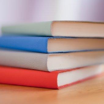 Hay sobre una superficie de madera cuatro libros apilados de colores. 