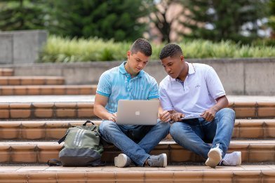 Dos estudiantes sentados en unas escaleras sosteniendo un computador portatil